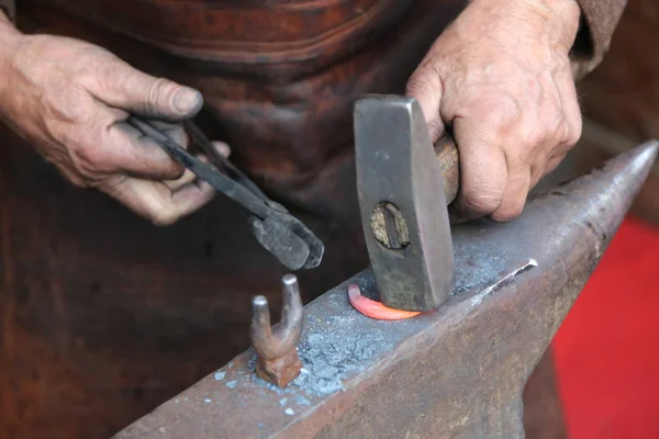 Рука старшего кузнеца, который использует плоскогубцы, чтобы сформировать горячее железо — стоковое фото