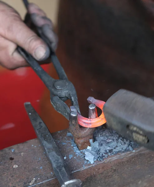Handen van een bejaarde smid bewerken van ijzer met een hamer en th — Stockfoto