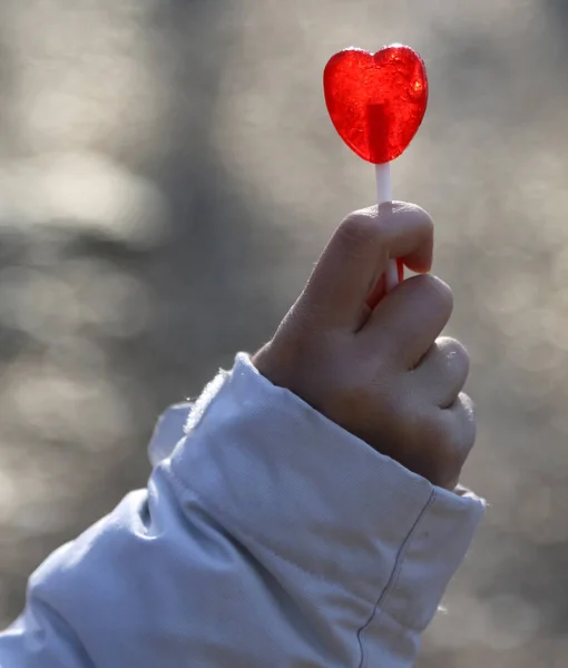 Bambino che tiene un lecca-lecca a forma di cuore rosso — Foto Stock