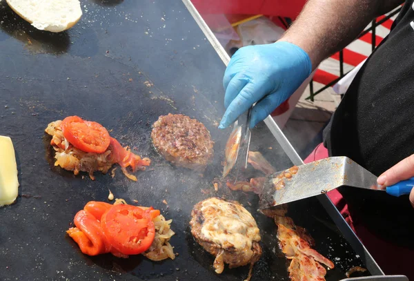 Chef com luvas azuis cozinhar hamburguer com tomates — Fotografia de Stock
