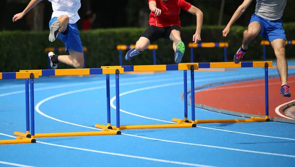 Drie jonge atleten tijdens het uitvoeren van horden op de atletiekbaan — Stockfoto