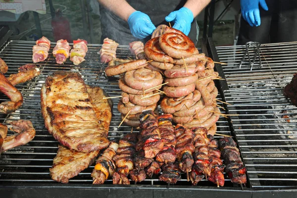 Geübter Koch mit blauen Handschuhen, der die Fleischspieße mit Pfeffer zubereitet — Stockfoto