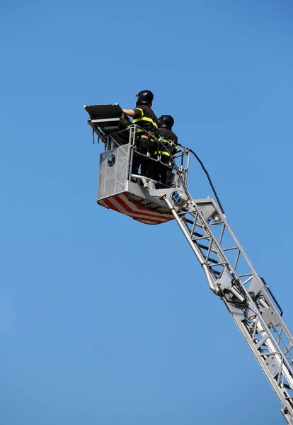 Two intrepid firefighters over the ladder truck metal basket dur — Stock Photo, Image