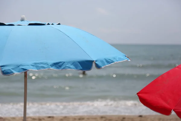 Guarda-sóis de praia azul e vermelho na praia junto ao mar no verão — Fotografia de Stock