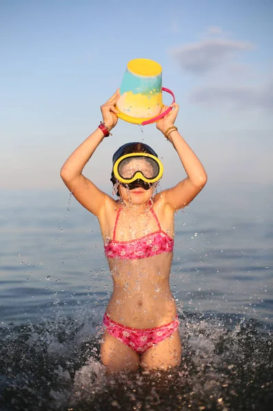 küçük kız mayo su dolu kova ile denizde çalış.