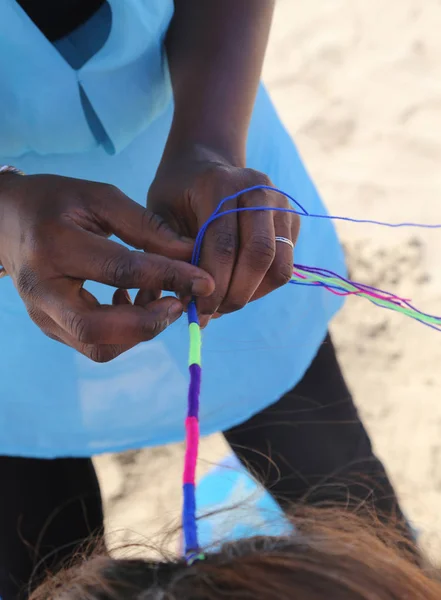 アフリカの女性が、海でカラフルな三つ編みの髪型を作る — ストック写真
