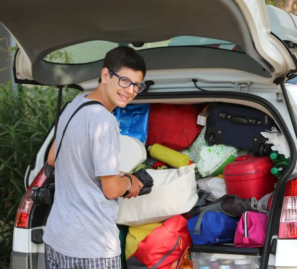 Jeune garçon avec des lunettes met des valises dans les bagages de la voiture — Photo