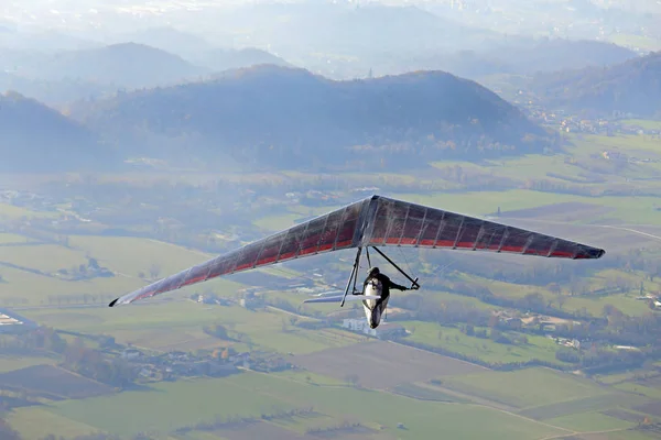 Hombre volando alto con su ala delta sobre la llanura — Foto de Stock