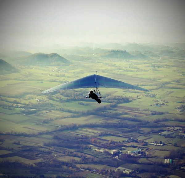 Hombre volando alto con su ala delta sobre la llanura — Foto de Stock