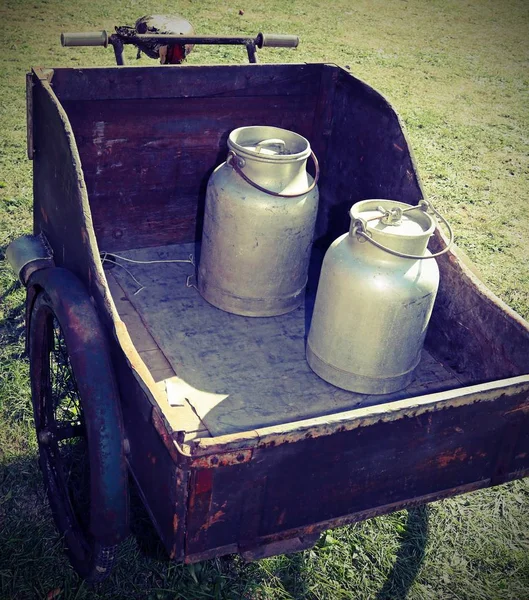 Latas de leite velhas transportadas por um vagão velho com bicicleta enferrujada — Fotografia de Stock