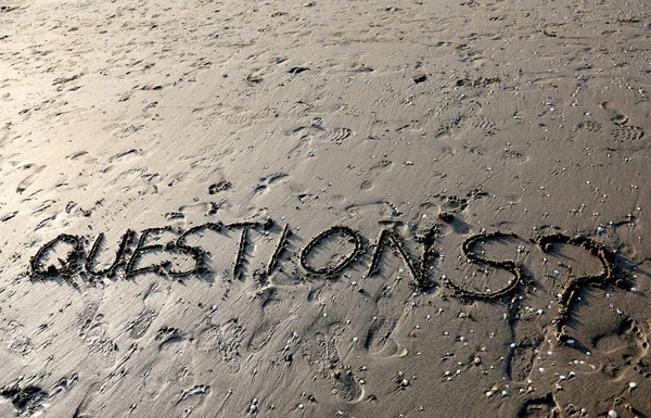 Textfrågor med frågetecken skriven på sanden — Stockfoto