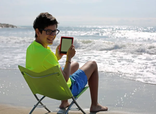 Garçon avec des lunettes lit un ebook sur la plage — Photo