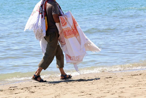 Vendedor com panos e tecidos caminha na praia ensolarada em suma — Fotografia de Stock