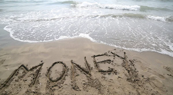 Texto DINERO en la arena y la ola que está borrando la palabra símbolo — Foto de Stock
