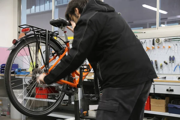 Homem na oficina de reparação de bicicletas com uma bicicleta laranja — Fotografia de Stock