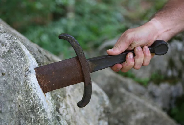 Hand of the knight trying to draw the sword into the rock — Stock Photo, Image
