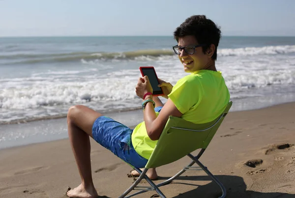 Jeune garçon avec ebook et short sur la plage en été — Photo