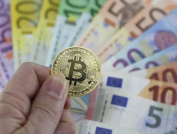 Ruka muže s jedním velkým goden Bitcoin a eurobankovek na bac — Stock fotografie