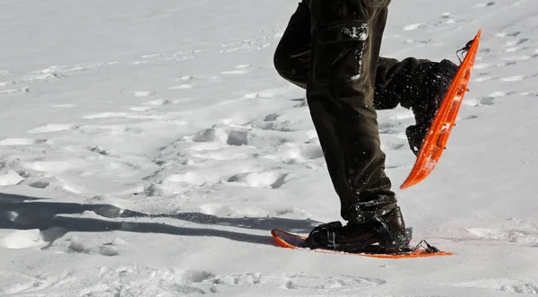 Man sneeuwschoenwandelen met oranje sneeuwschoenen — Stockfoto