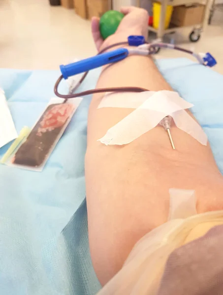 Aguja en el brazo y joven voluntario durante la donación de sangre — Foto de Stock