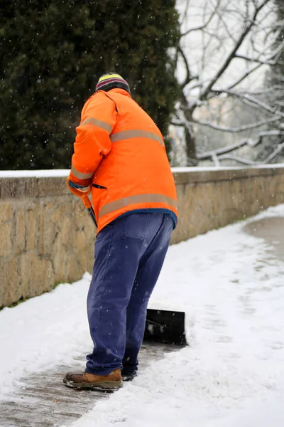 Onderhoud werknemer terwijl hij schoppen de sneeuw van het trottoir — Stockfoto