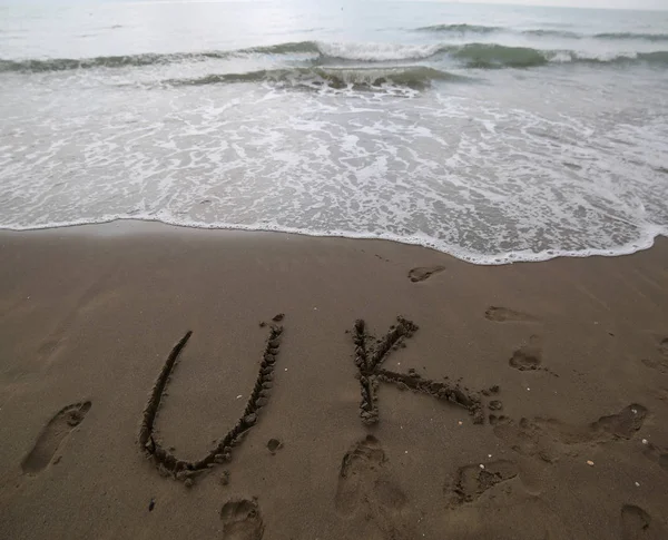 Texto del Reino Unido escrito en la arena de la playa cerca del mar —  Fotos de Stock