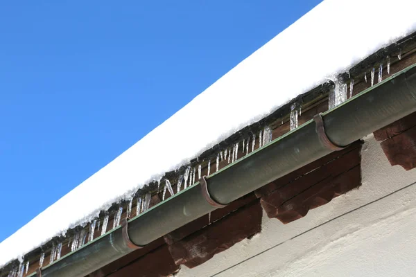 Grondaia con ghiaccioli di ghiaccio sul tetto dopo copiose nevicate — Foto Stock