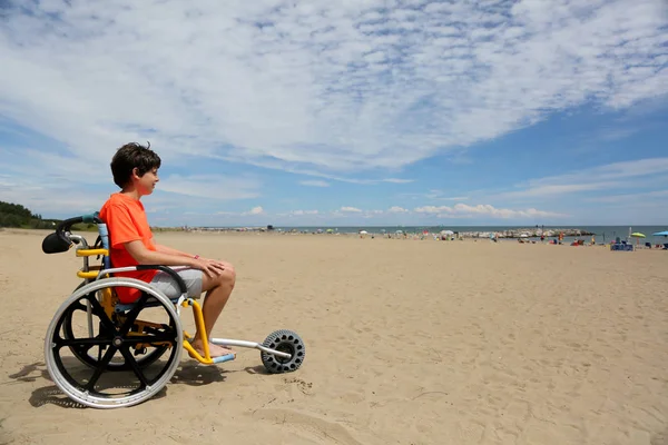 Niño con camiseta naranja sentado en la silla de ruedas especial con un —  Fotos de Stock