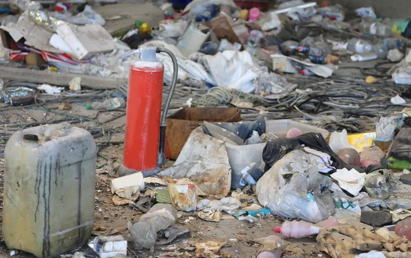 Red extinguisher in a homeless shelter with many garbage — Stock Photo, Image
