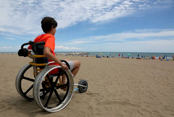 Ragazzo guarda il mare da una sedia a rotelle — Foto Stock