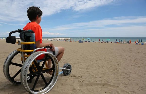 Turuncu tişört ile özel tekerlekli sandalye üzerinde oturan çocukla bir — Stok fotoğraf