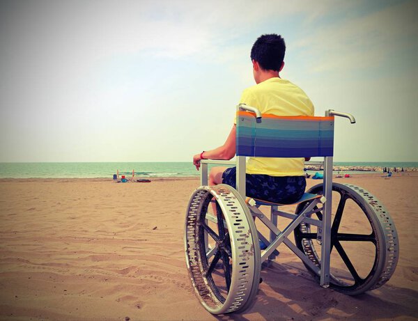 boy on a wheelchair looks at the sea