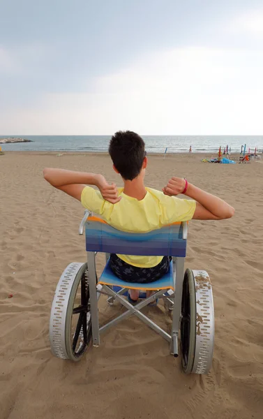 Garçon handicapé dans un fauteuil roulant lokks à la mer — Photo