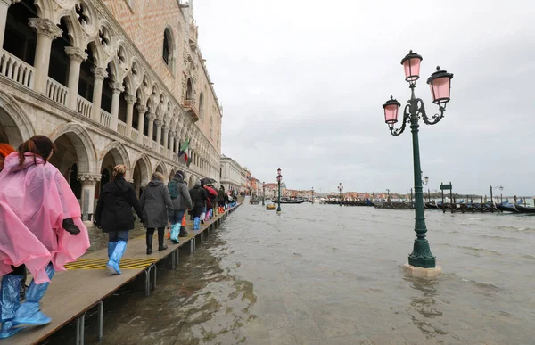 Many people on the footbridge with plastic gaiters in Venice in — Stock Photo, Image