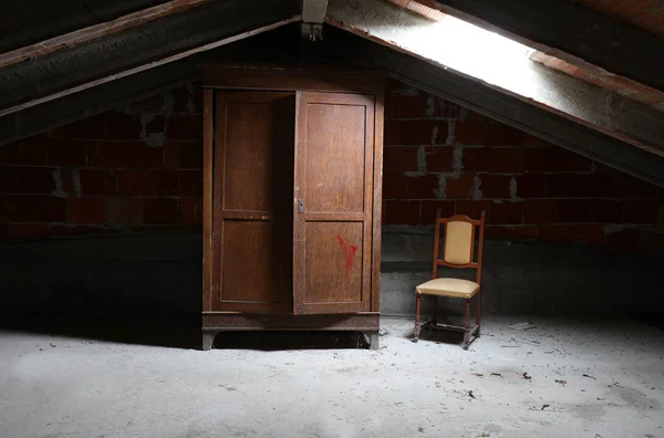 Old wooden wardrobe and a vintage chair in the dusty attic — Stock Photo, Image