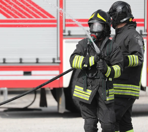 Bomberos con manguera hidrante en acción y bombero —  Fotos de Stock