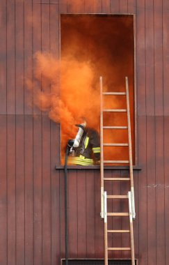 İtfaiyeci, oksijen tüpüyle zehirli turuncu dumanla dolu binaya giriyor.