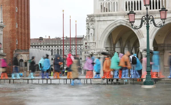 many people walk on a catwalk in Venice due to the high tide