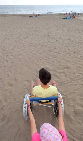Menina Empurra Irmão Deficiente Uma Cadeira Rodas Praia — Fotografia de Stock