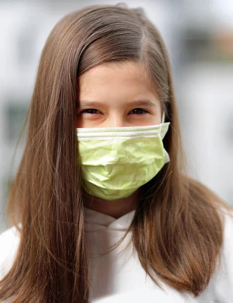 髪の長い若い女の子はコロナウイルスから呼吸器を保護するために外科マスクを身に着けています — ストック写真