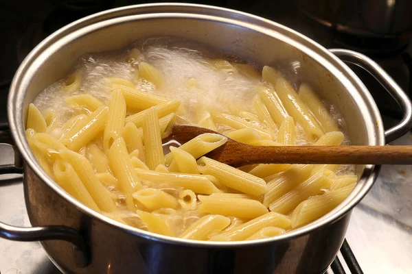 锅里有开水和意大利面 还有一个木制勺子来搅拌 — 图库照片