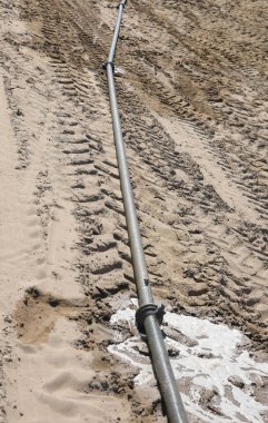 Kurak mevsimde sıcak yaz mevsiminde ekili tarlayı sulamak için uzun metalik hortum.