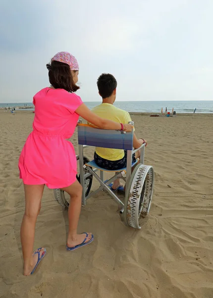 Dość Kaukaskie Mała Dziewczynka Popycha Wózku Inwalidzkim Jej Brat Piaszczystej — Zdjęcie stockowe