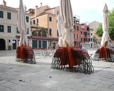 Tables and chairs of an alfresco cafe without tourists in Venice in Italy due to the Corona Virus epidemic that has blocked borders clipart