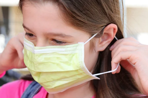 女の子は致命的なウイルス冠から保護するために耳の後ろの弾性を持つ緑色の外科用マスクを正しく身に着けています — ストック写真
