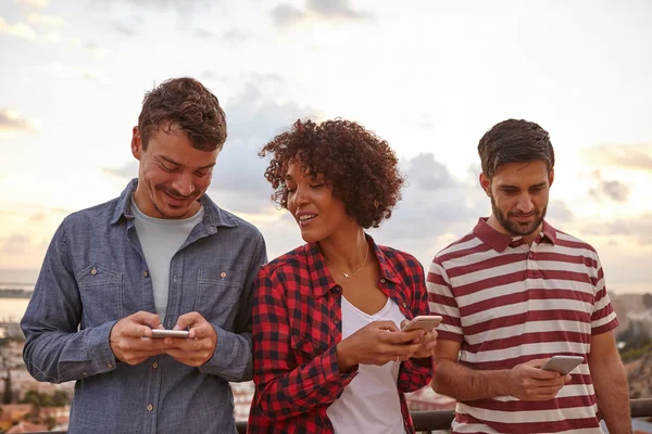 Tres amigos mirando teléfonos celulares — Foto de Stock