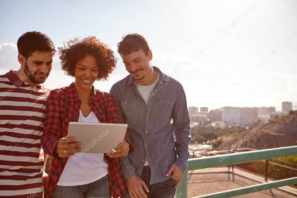 Three smiling friends looking at  tablet