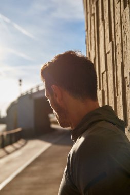 Duvara yaslanmış bir adam yan tarafa bakıyor.