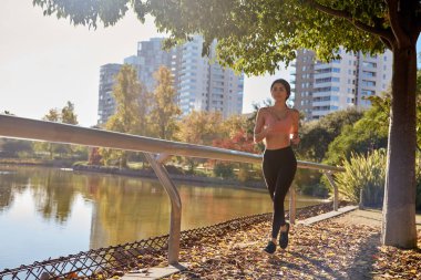 Genç bir kadın bir ağacın yanından koşarak geçiyor.
