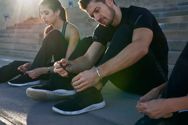 Seated man lifts his knees as he adjusts his laces